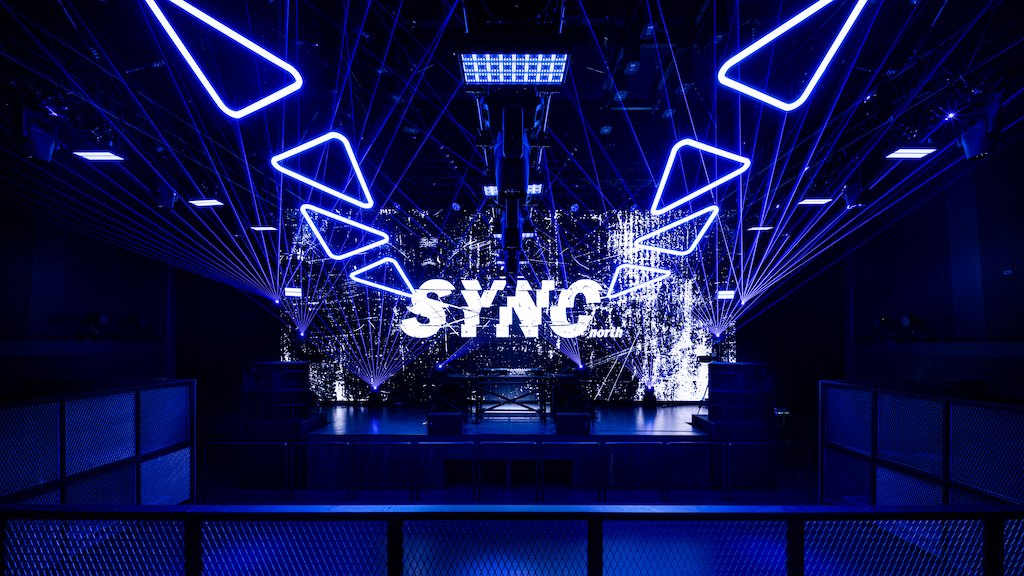 The main floor under blue light, with the SYNC north logo on the LED wall behind the stage