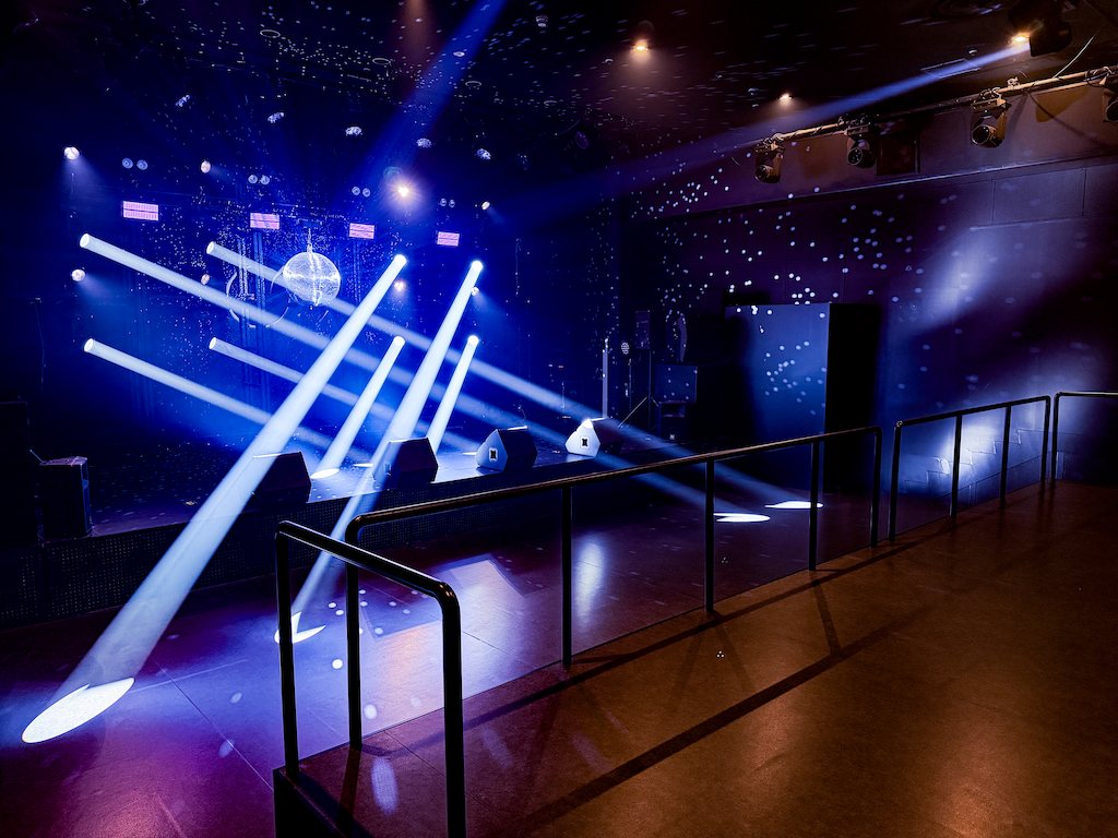B1F LEGACY FLOOR seen over the railing: the floor and stage, blue beams across the floor