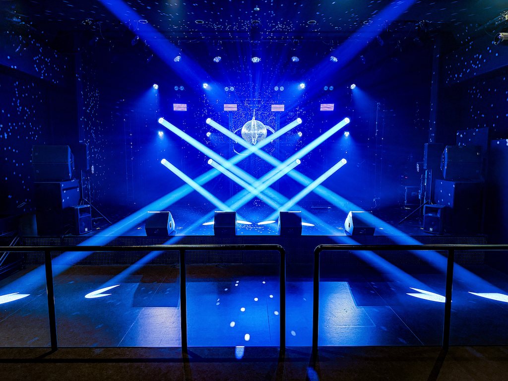 The stage of B1F LEGACY FLOOR: crossing blue moving-light beams and a mirror ball at the centre