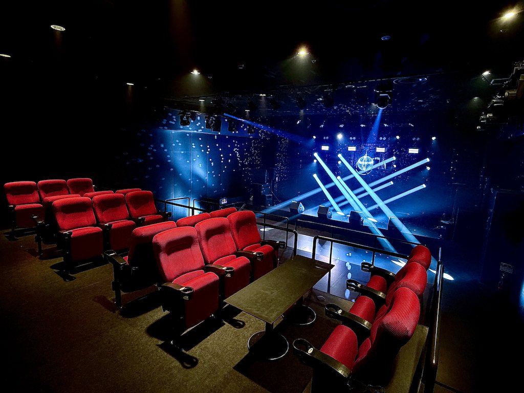 B1F LEGACY FLOOR: tiers of red seats reused from the cinema, the blue-lit stage beyond