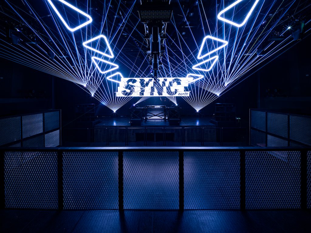 The main floor seen over the mesh railing: the LED sign ahead and blue lasers fanning out from the ceiling