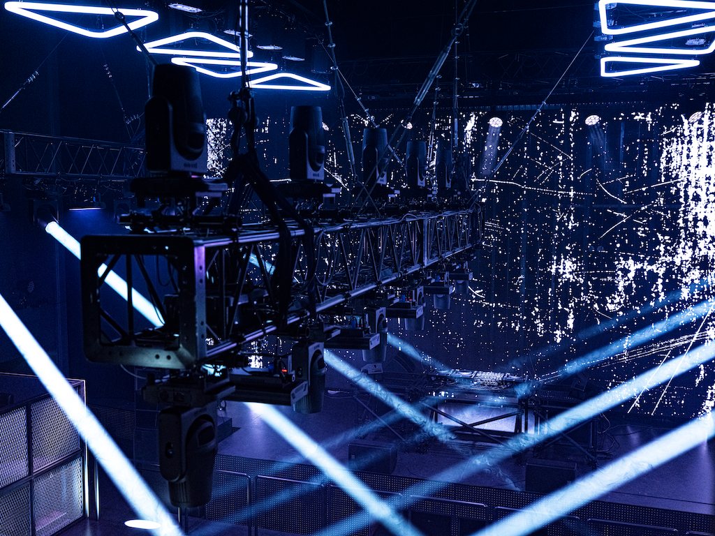Moving lights hung from a truss, casting pale blue beams