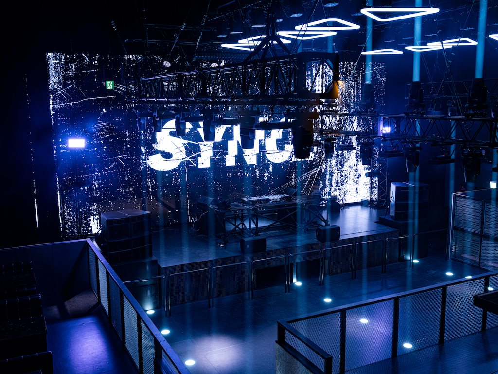 The floor seen over the upper railing: the SYNC north logo on the LED wall, blue light on the floor