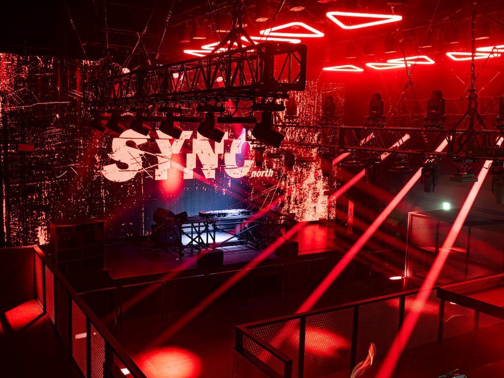 The floor and trusses washed in red light, the SYNC north logo behind