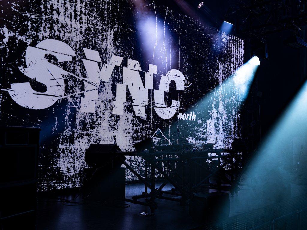 The SYNC north logo filling the LED wall, a spotlight on the stage