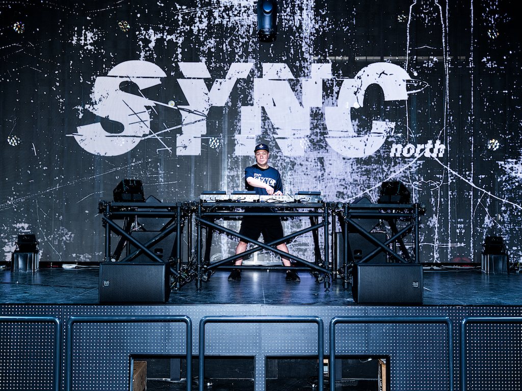 The DJ booth on stage in front of the SYNC north logo on the LED wall