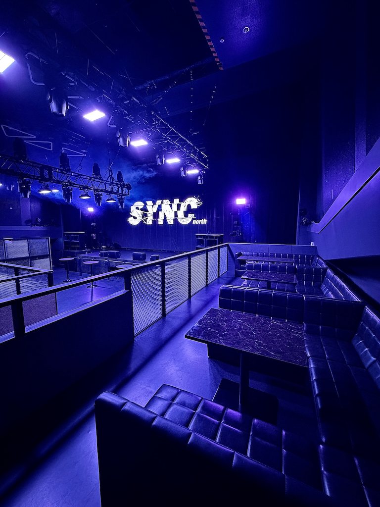 VIP seating facing the main floor: leather sofas and marble tables, the floor and the stage LED sign beyond the railing