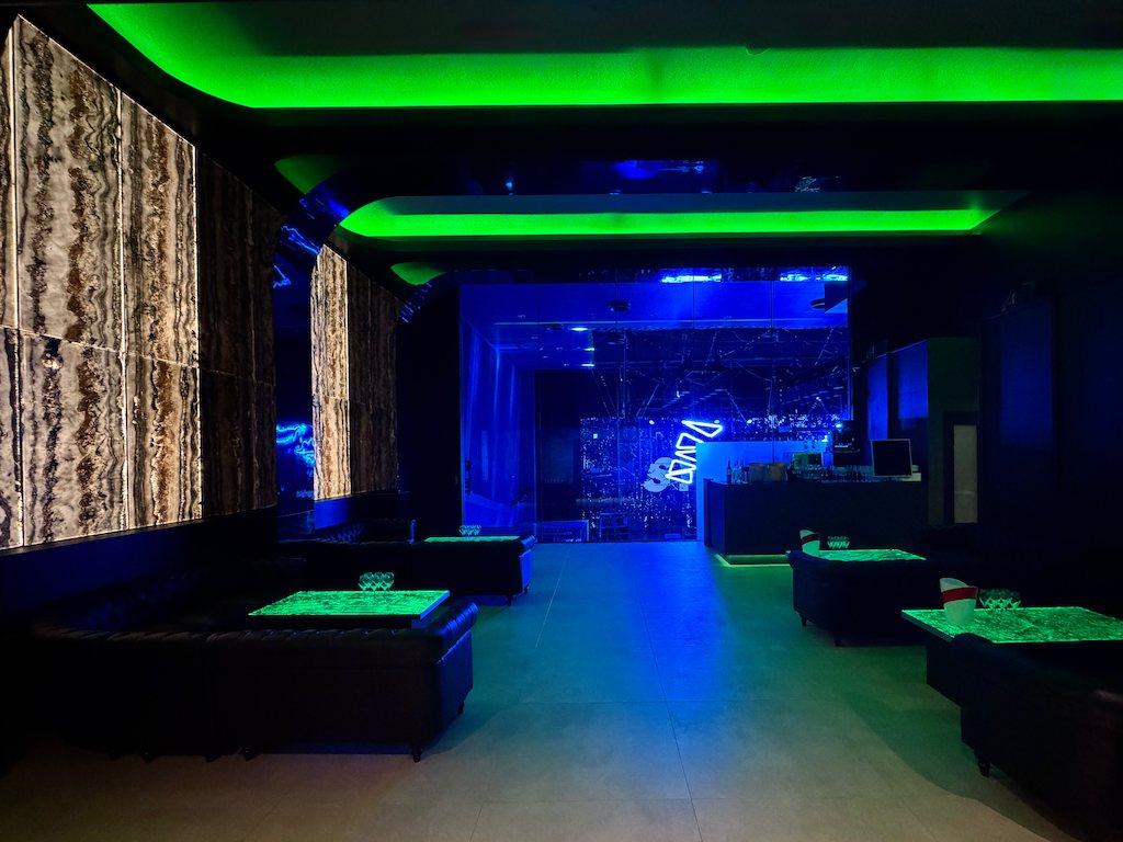 3F VVIP ROOM: sofa seating and tables between green cove lighting and onyx walls, the main floor visible through the glass at the back